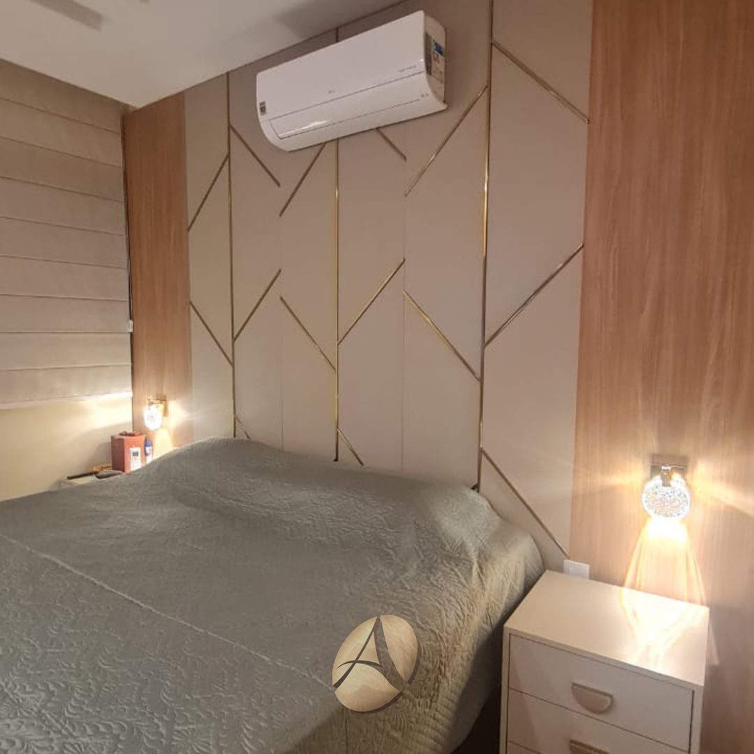 Quarto com paredes revestidas em espelhos formando ângulo, cama de casal com colcha cinza, poltrona lateral e luminária pendente em dourado